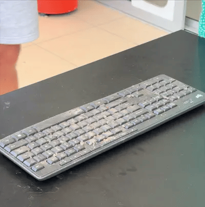 a person using a blowy v3 power blower blowing dust off of a dirty pc keyboard